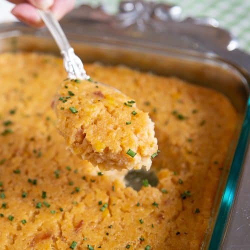 spoon scooping scalloped corn out of a casserole dish.