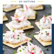 saltine crackers with crab dip on top, garnished with radish sticks and chopped chives.