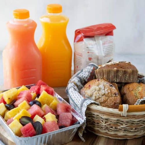 muffins, juice, fresh fruit, and coffee on a wooden platter.