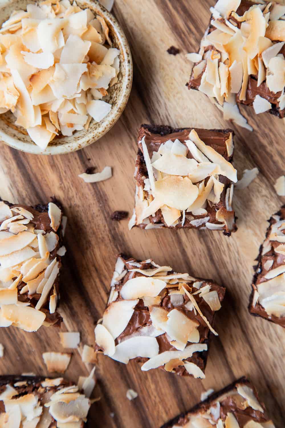 Brownies with frosting and toasted coconut on a wooden board