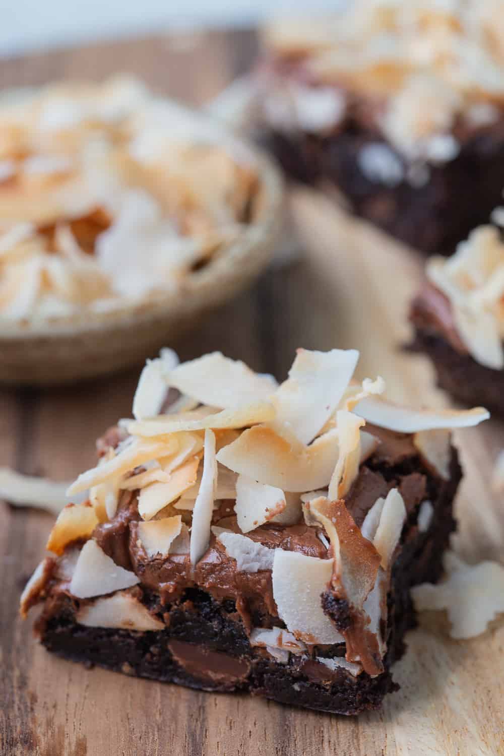 brownies topped with frosting and toasted coconut curls on a wooden board