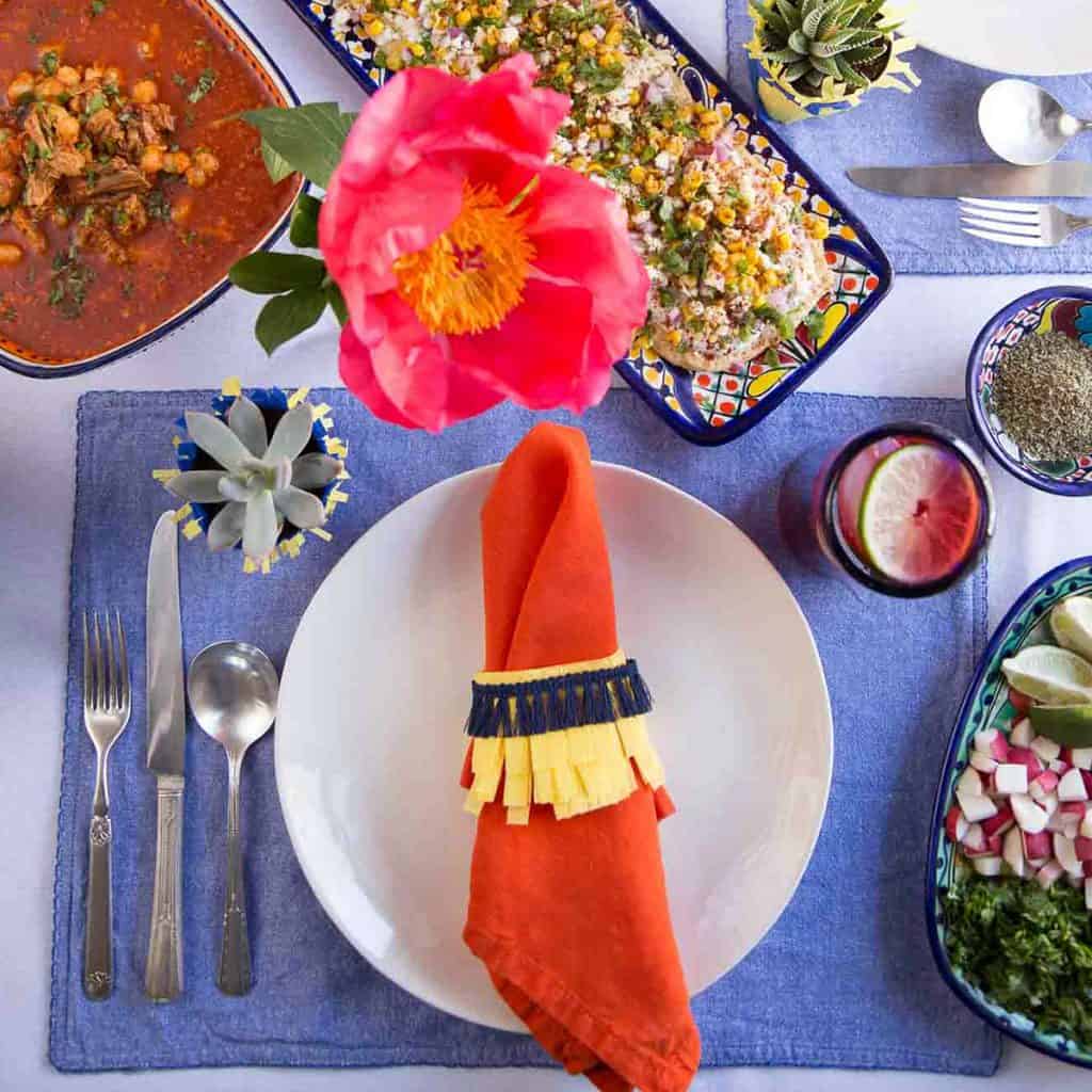 colorful table set for a cinco de mayo celebration, with a blue placemat, orange napkin, and a blue and yellow napkin ring.