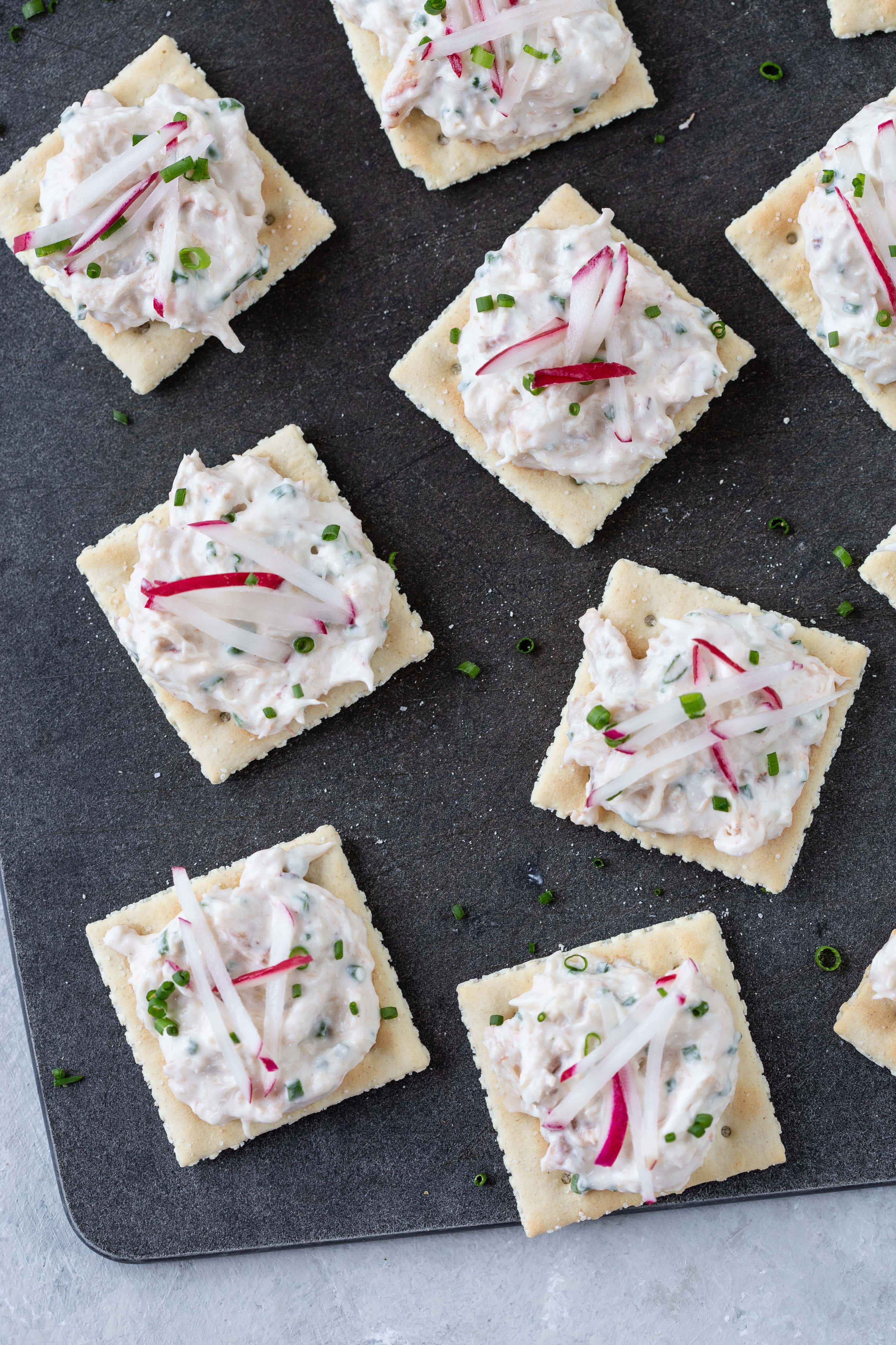 saltine crackers topped with crab dip and radishes on a black board