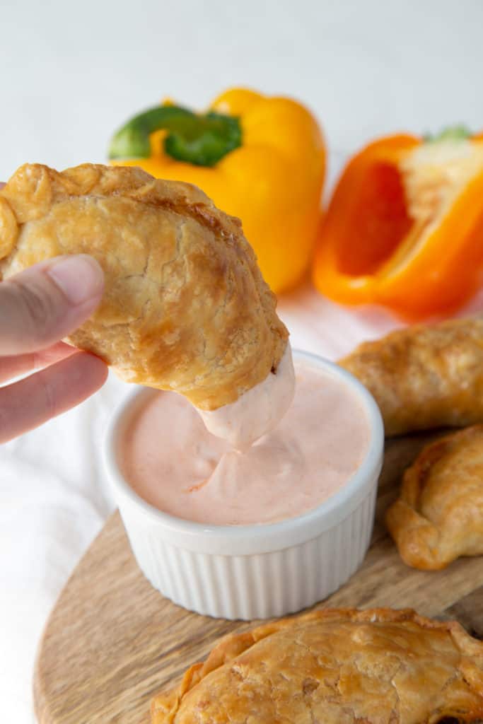 hand dipping an empanada in an orange dipping sauce.