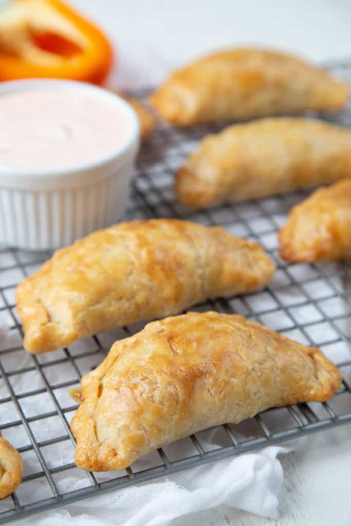 cooked Chicken Enchilada Empanadas on a wire rack with a white ramekin of dipping sauce.