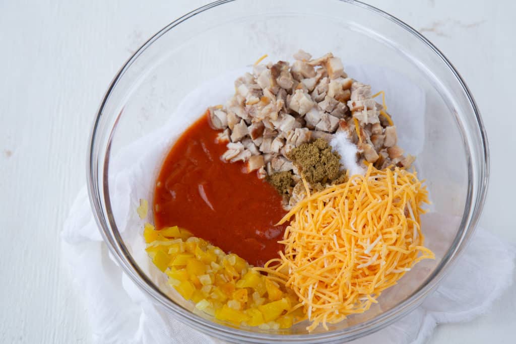 glass bowl filled with chicken, cheese, peppers, cumin, and enchilada sauce.
