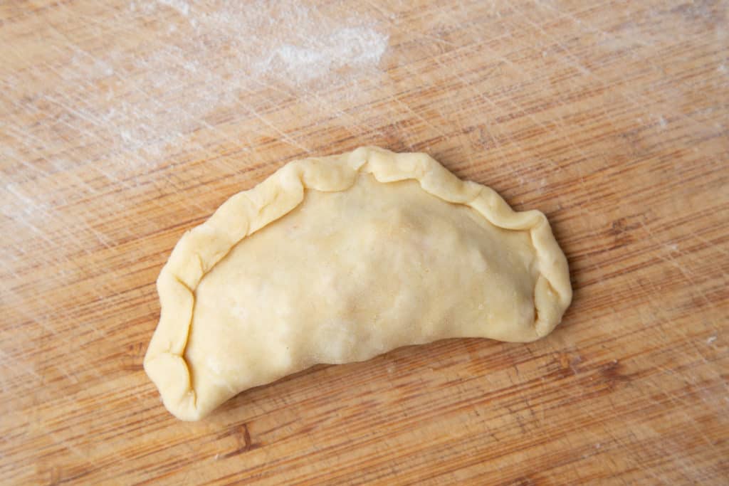 Unbaked empanada on wooden board.