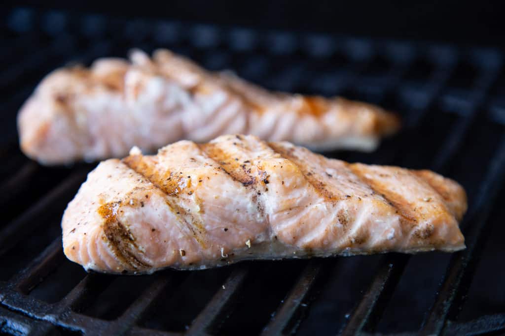 Two partially cooked salmon fillets on grill