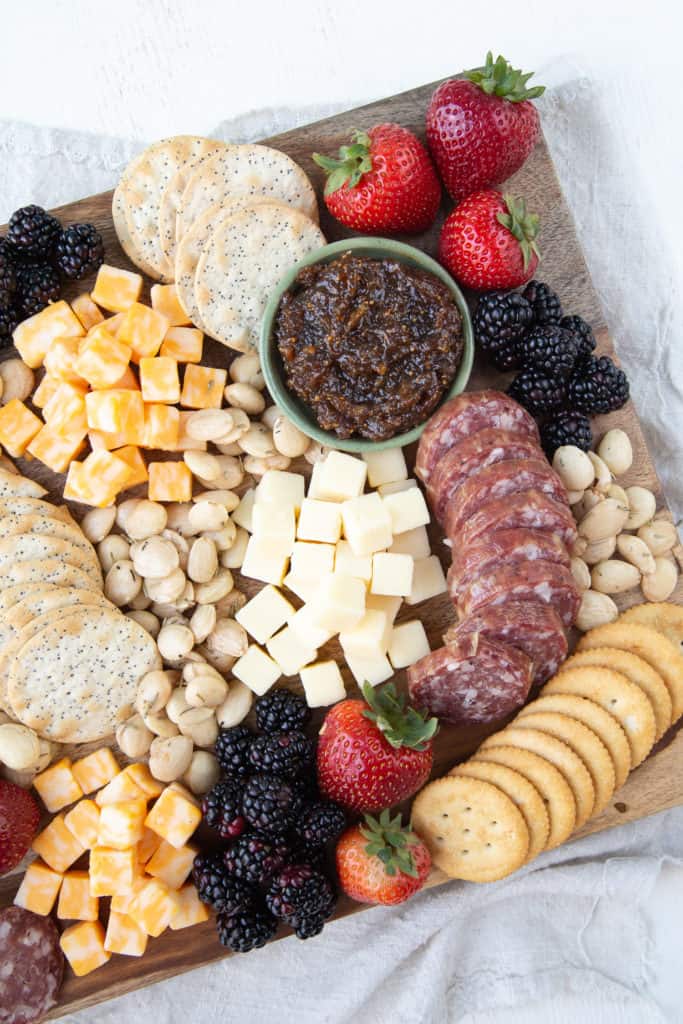 cheese, crackers, fruit, and nuts on a wooden board