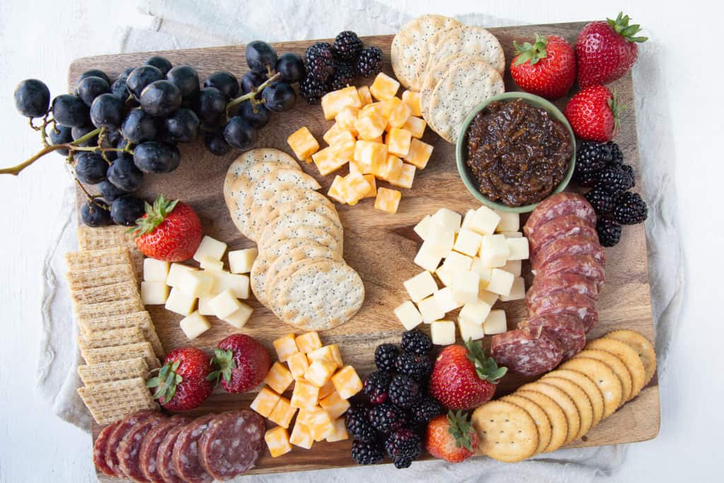 Wooden board with cheese, salami, crackers, and fruit