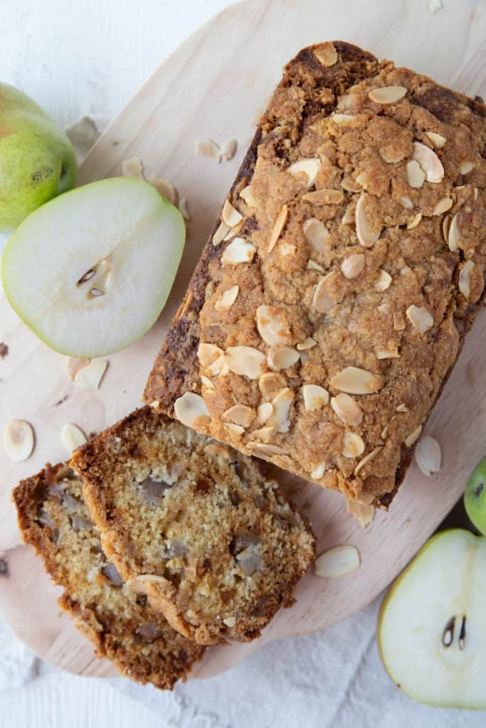 Pear Bread with slices cut out sitting on a wooden board with pear halves in the background