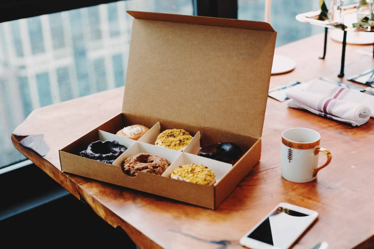 box of six artisan donuts on a table with a coffee mug and a smart phone.