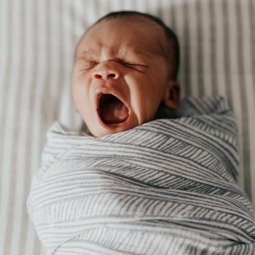 baby wrapped in a blue and white swaddle, yawning.