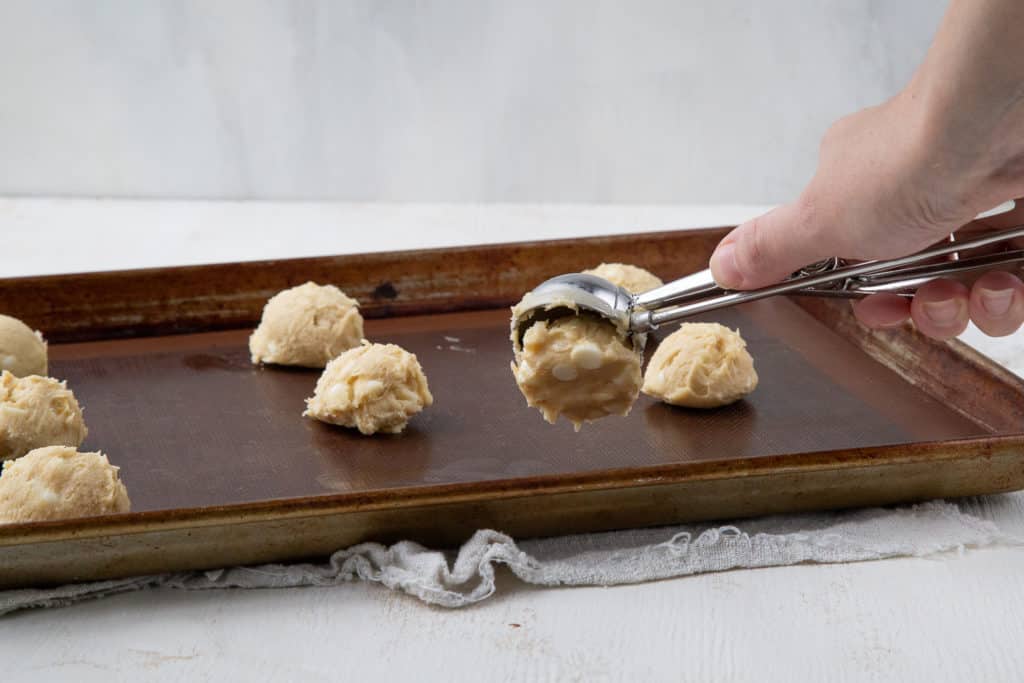 hand scooping cookie dough with a cookie scoop onto a baking sheet.