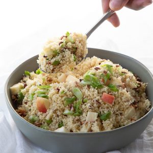 hand lifting up a spoonful of couscous with apples and pecans.
