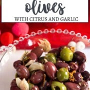 green and black olives with citrus zest and crushed garlic in a decorative glass bowl.
