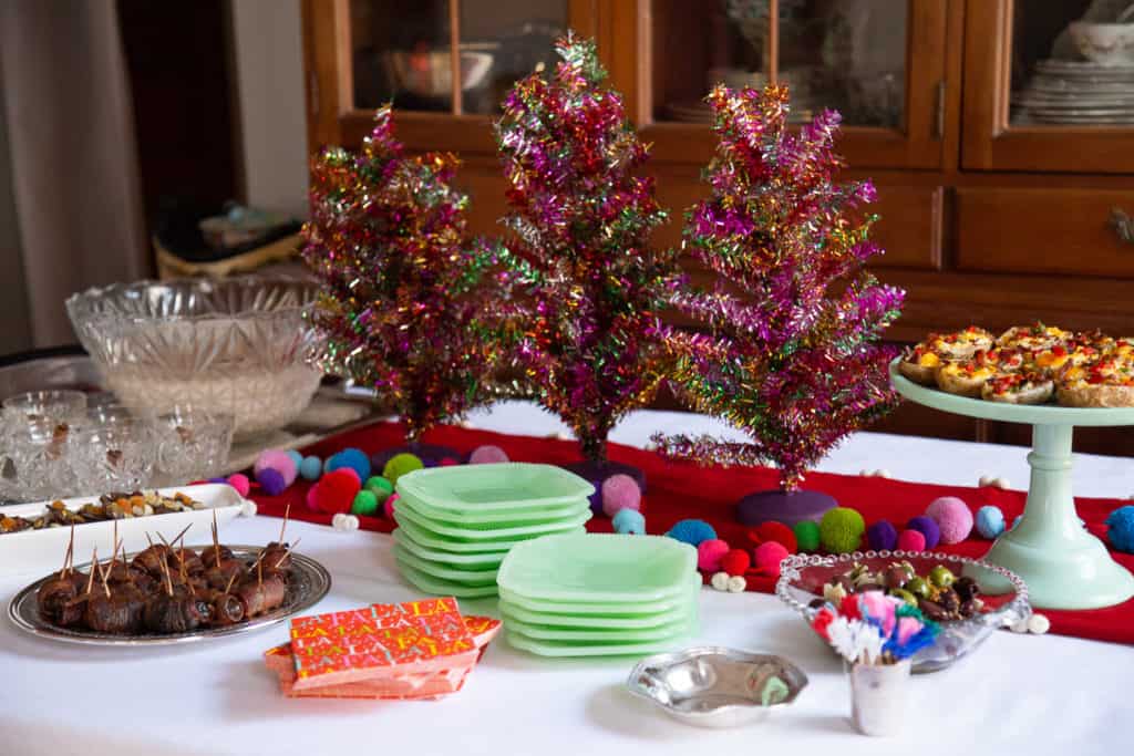 Holiday appetizer buffet with platters of appetizers, a punch bowl, and metallic tinsel tabletop trees