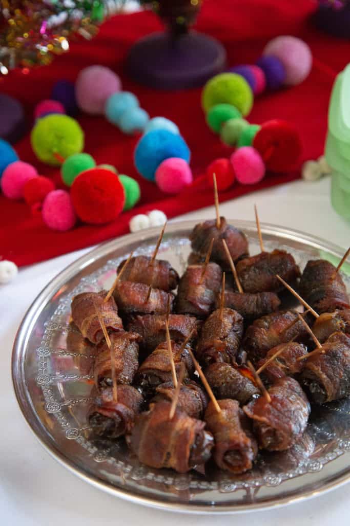 Boozy bacon wrapped dates on a silver platter on a holiday themed table.