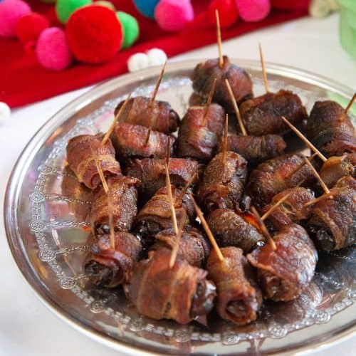 bacon wrapped dates with toothpicks on a round metal tray.