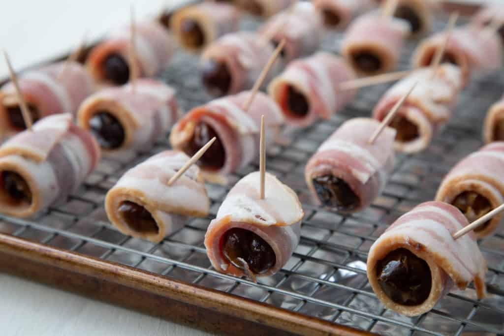 Uncooked bacon wrapped dates on a wire rack