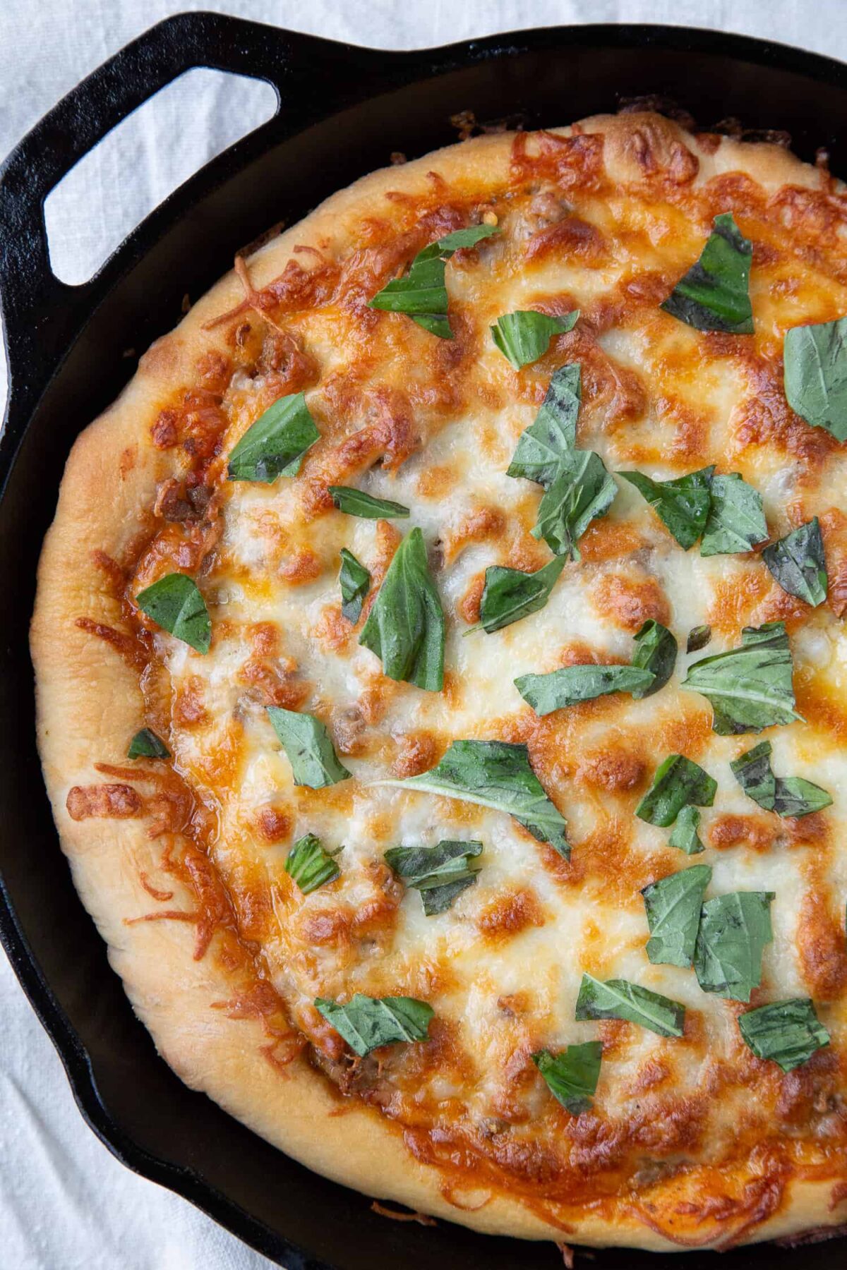 cast iron skillet pizza topped with pieces of fresh basil.