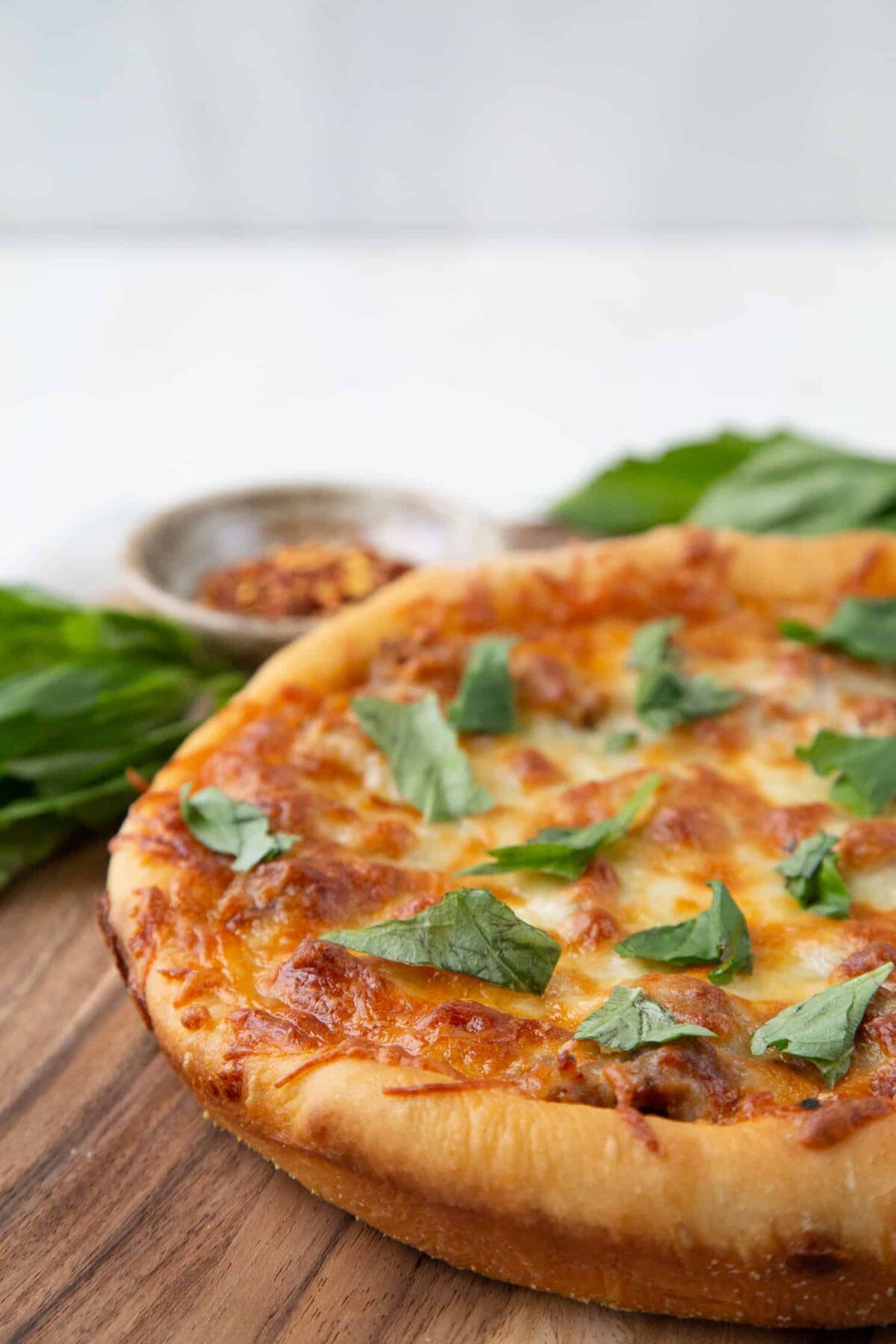 deep dish pizza topped with fresh basil on a wooden cutting board.