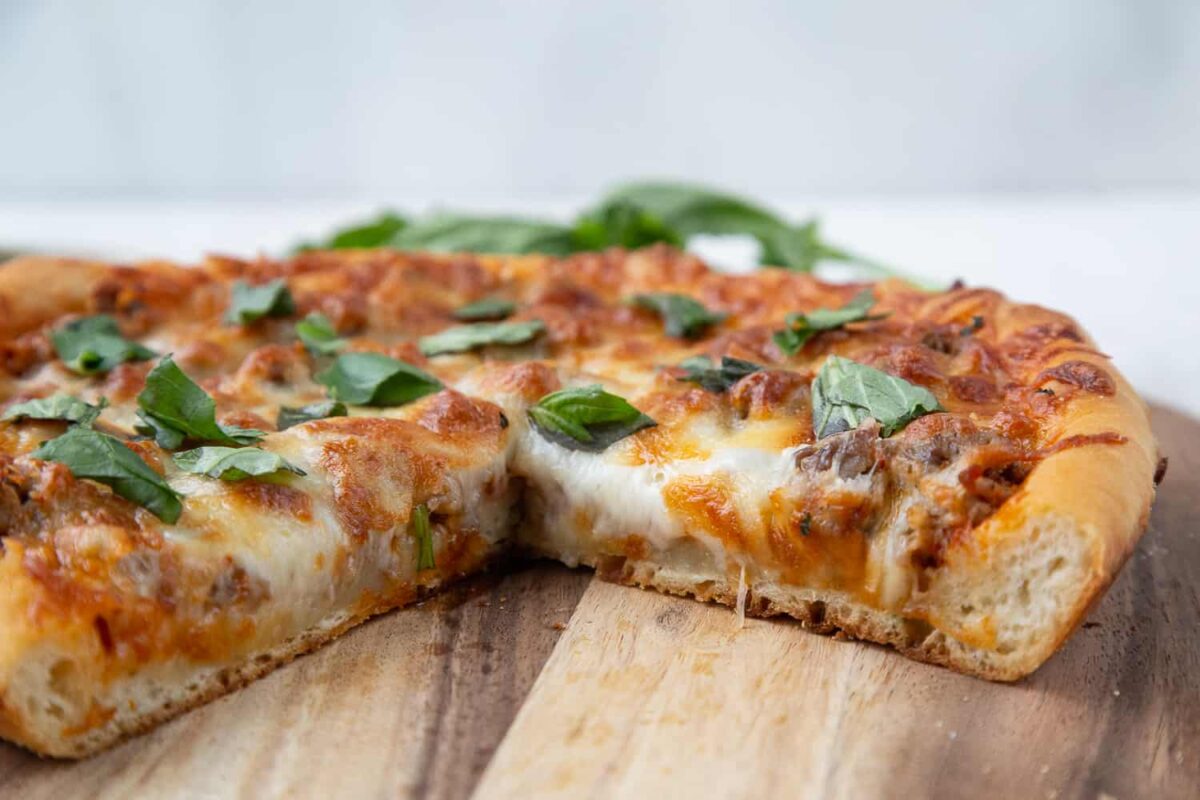 Cast iron skillet pizza on a wooden cutting board with slices taken out