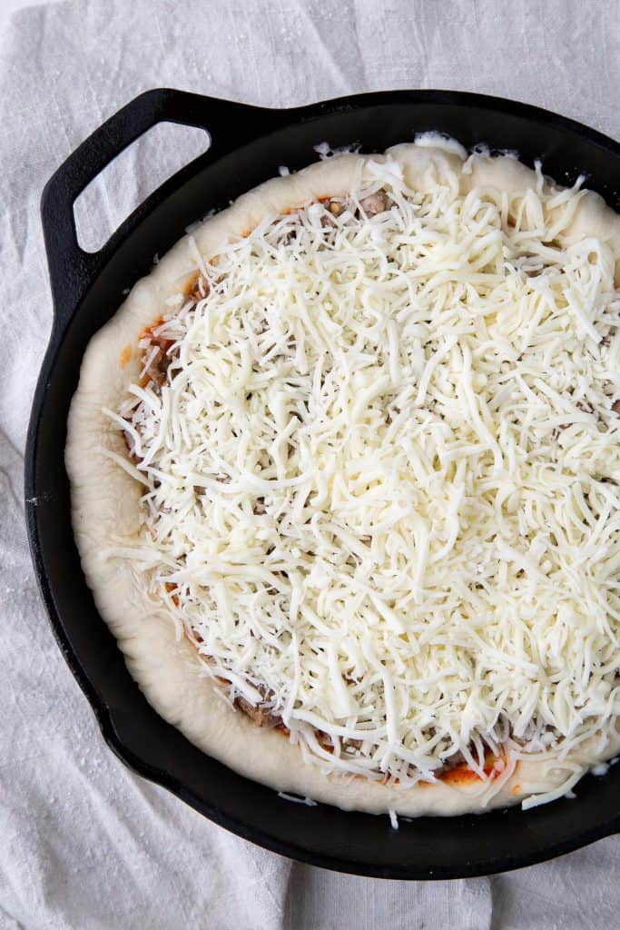 Uncooked pizza with lots of cheese in a cast iron skillet