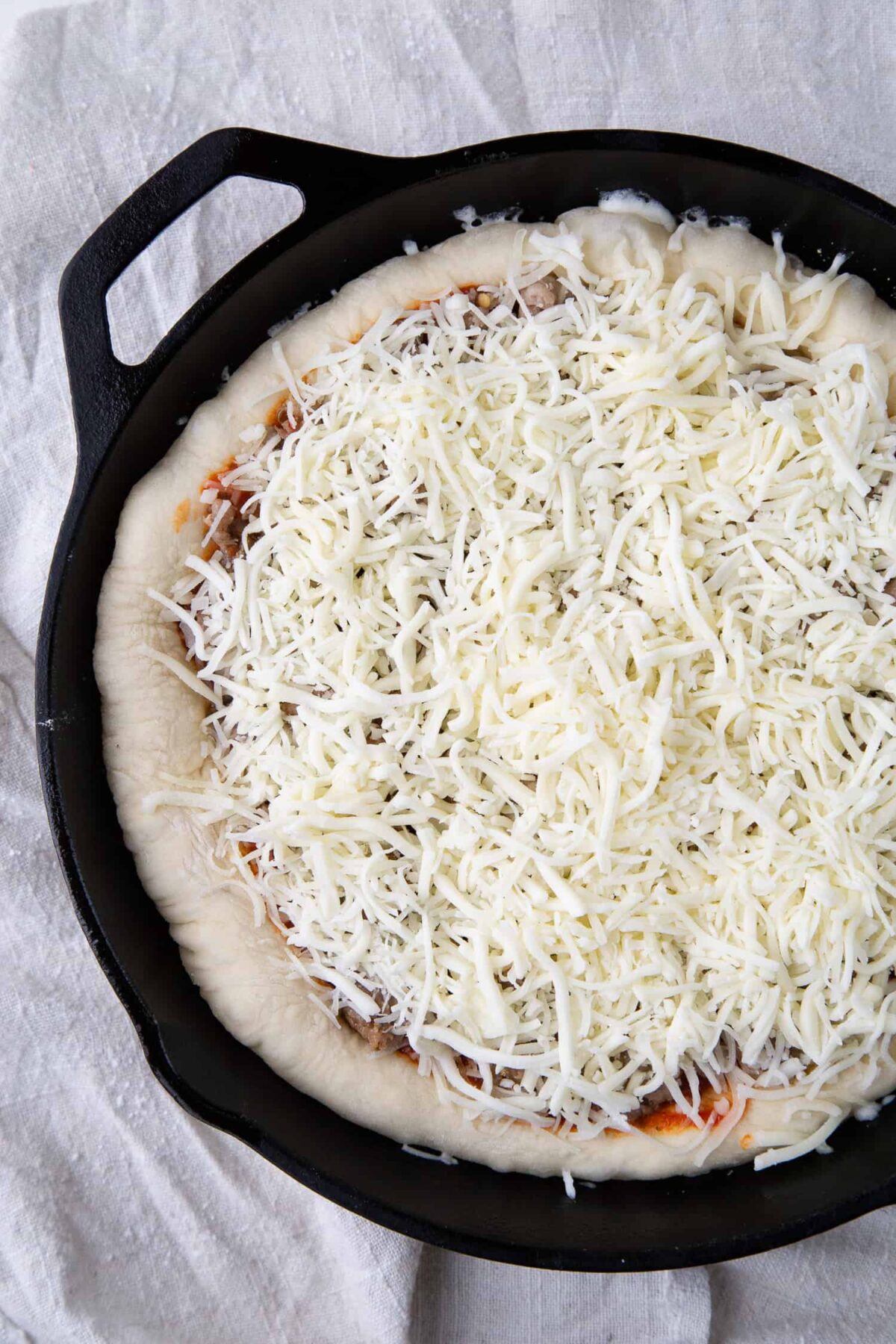 Uncooked pizza with lots of cheese in a cast iron skillet.