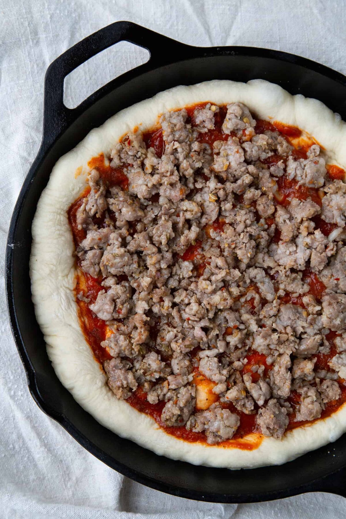 uncooked pizza with sausage in a cast iron skillet