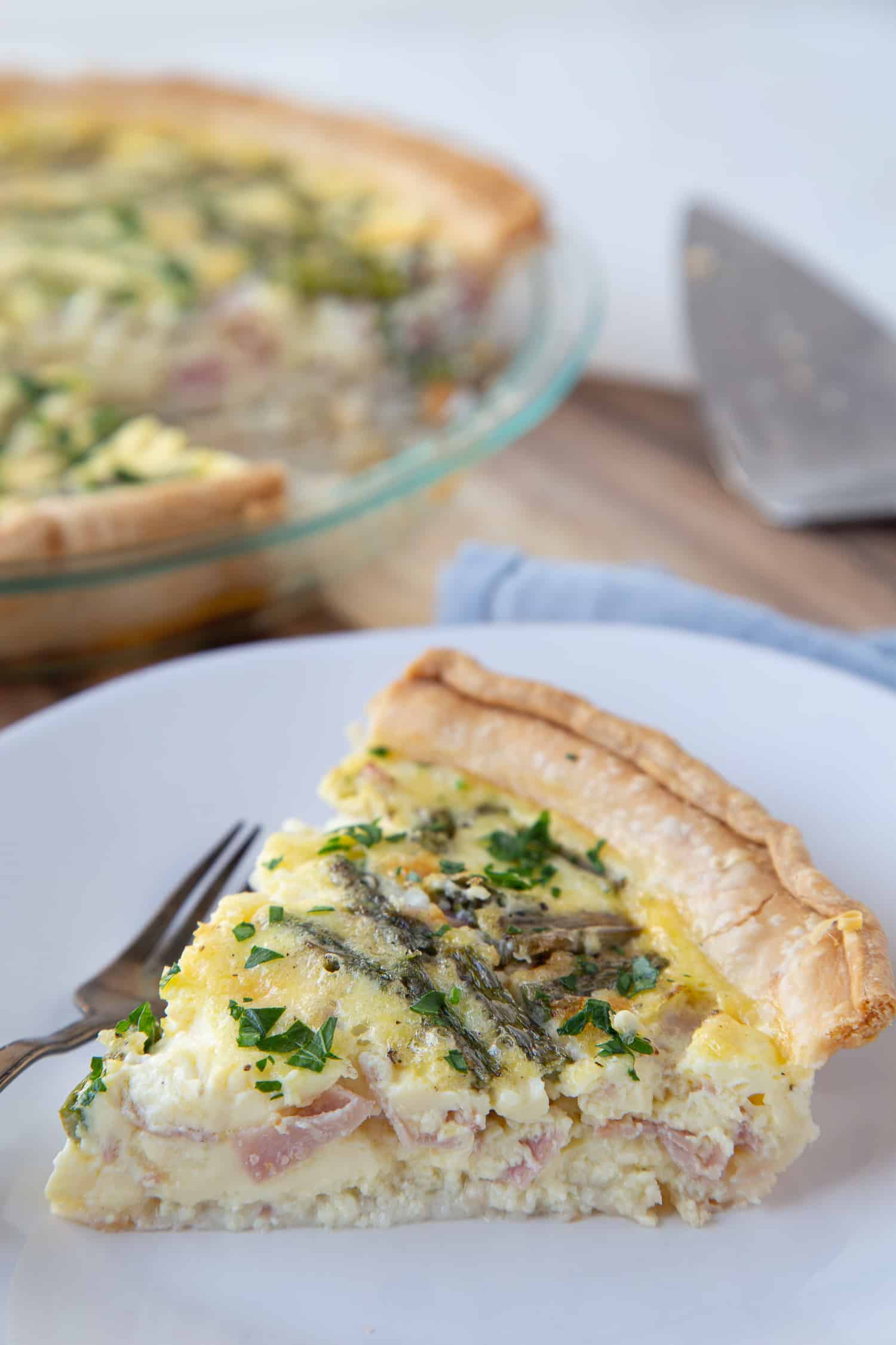 slice of asparagus and ham quiche on a white plate with a fork.
