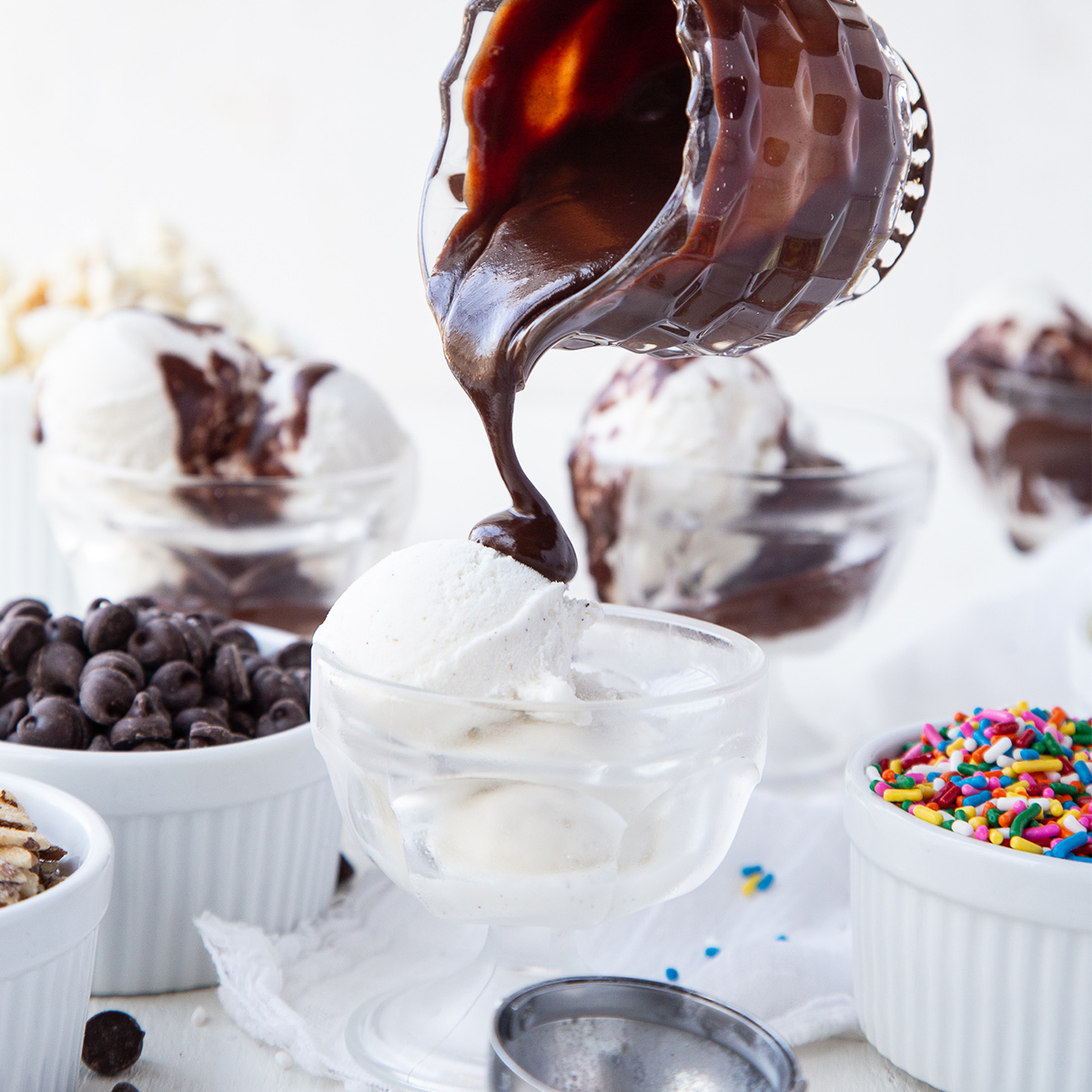 hand pouring hot fudge on a glass dish of vanilla ice cream