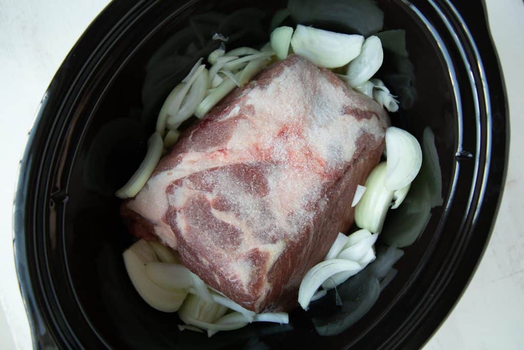 raw pork shoulder and onions in a slow cooker.