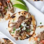 Carnitas on a white platter with lime wedges