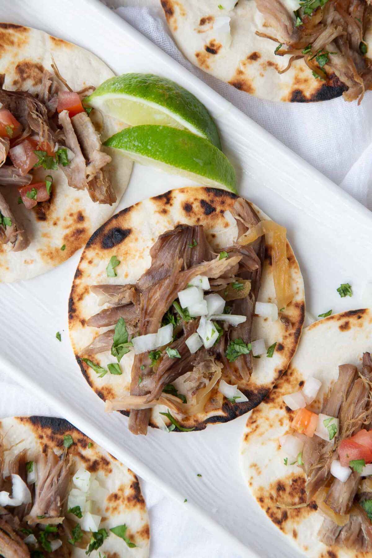 Carnitas on a white platter with lime wedges.