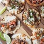 Mini tortillas stuffed with pork and pico de gallo on a round wooden board