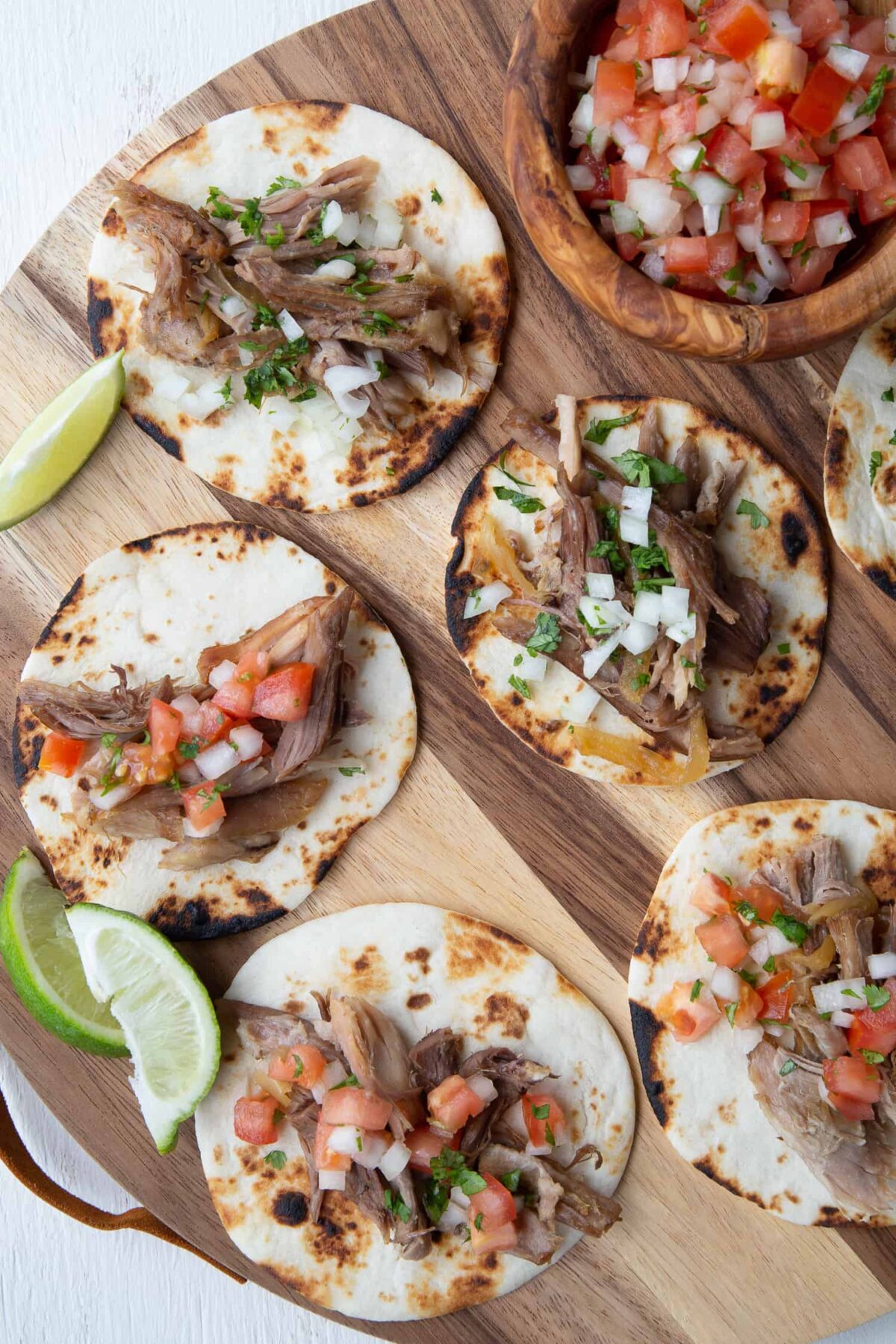 Mini tortillas stuffed with pork and pico de gallo on a round wooden board.