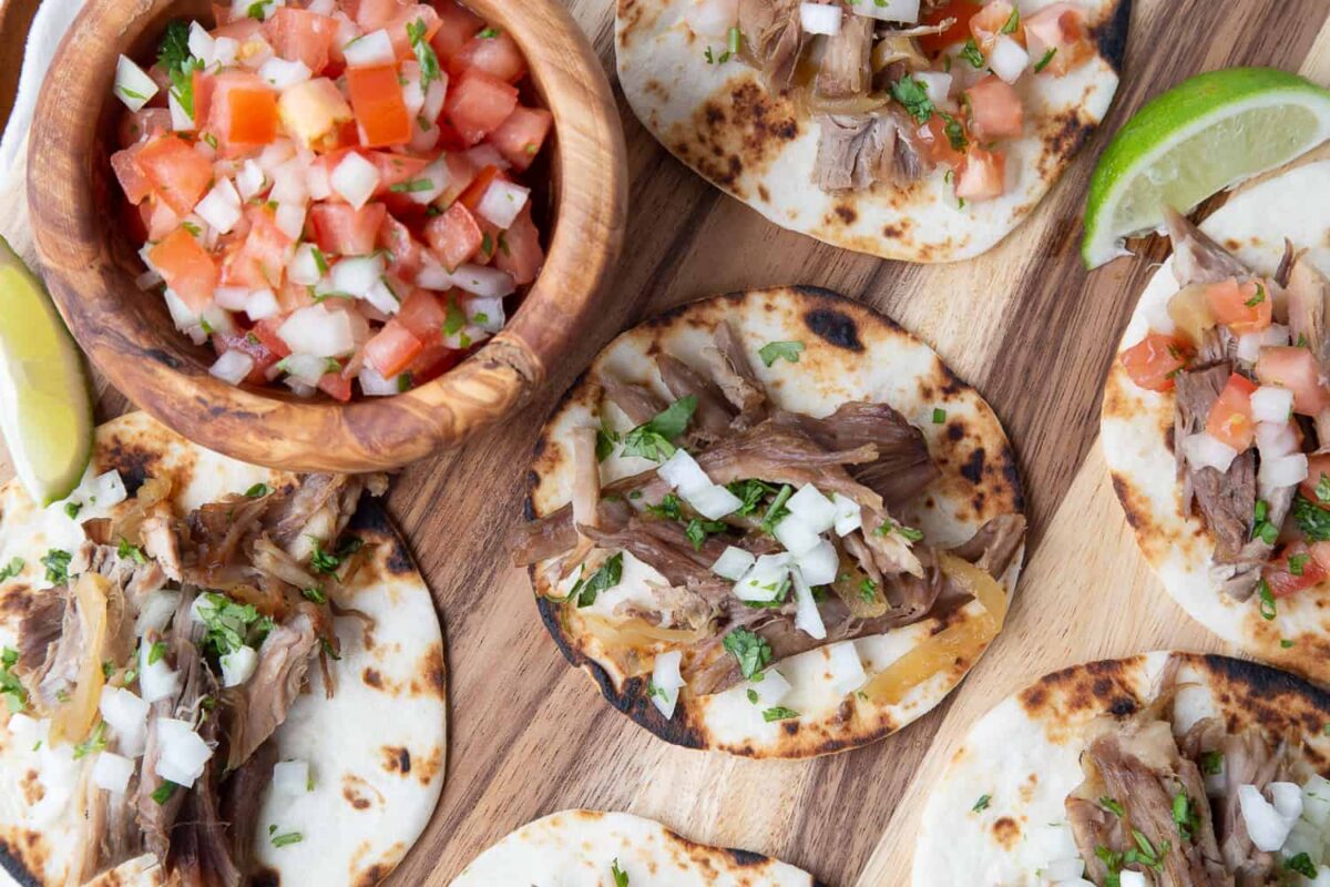 carnitas on mini flour tortillas with a wooden bowl of pico de gallo.