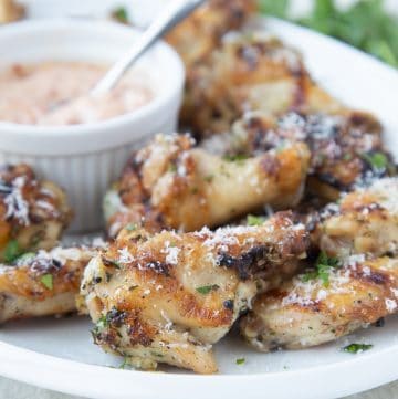 Grilled wings on a white platter with sun dried tomato dipping sauce