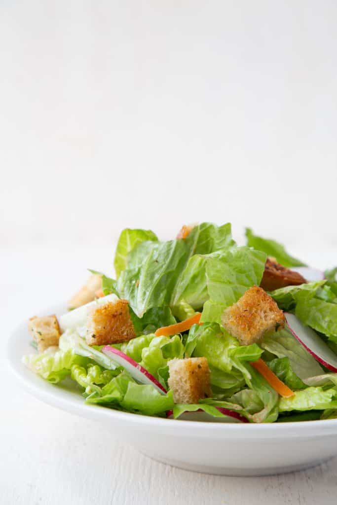 Leafy green salad with croutons in a white bowl