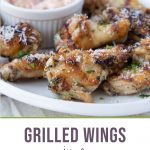 Garlic and herb wings on a white platter with a small white bowl of sun dried tomato mayo