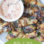 Garlic and herb wings on a white platter with a small white bowl of sun dried tomato mayo