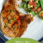 grilled glazed pork chop on a white plate with a side of summer veggies