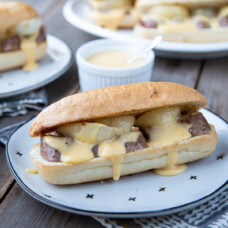 bratwurst sandwich with cheese sauce on a white plate