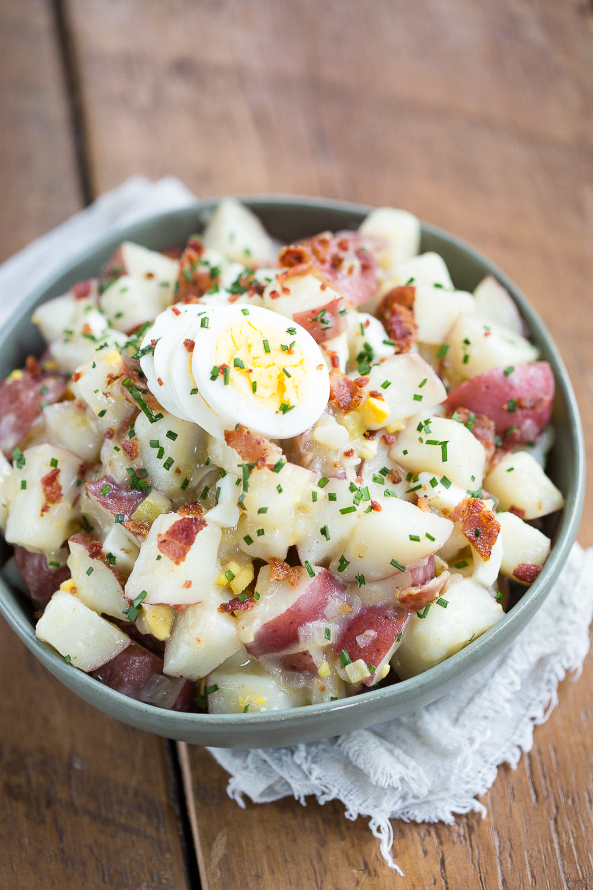 german potato salad with eggs in a green bowl.