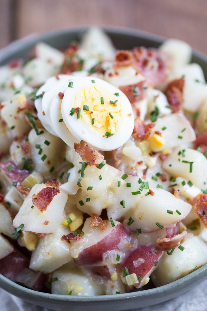 german potato salad with hard boiled eggs and chives for garnish, in a green serving dish