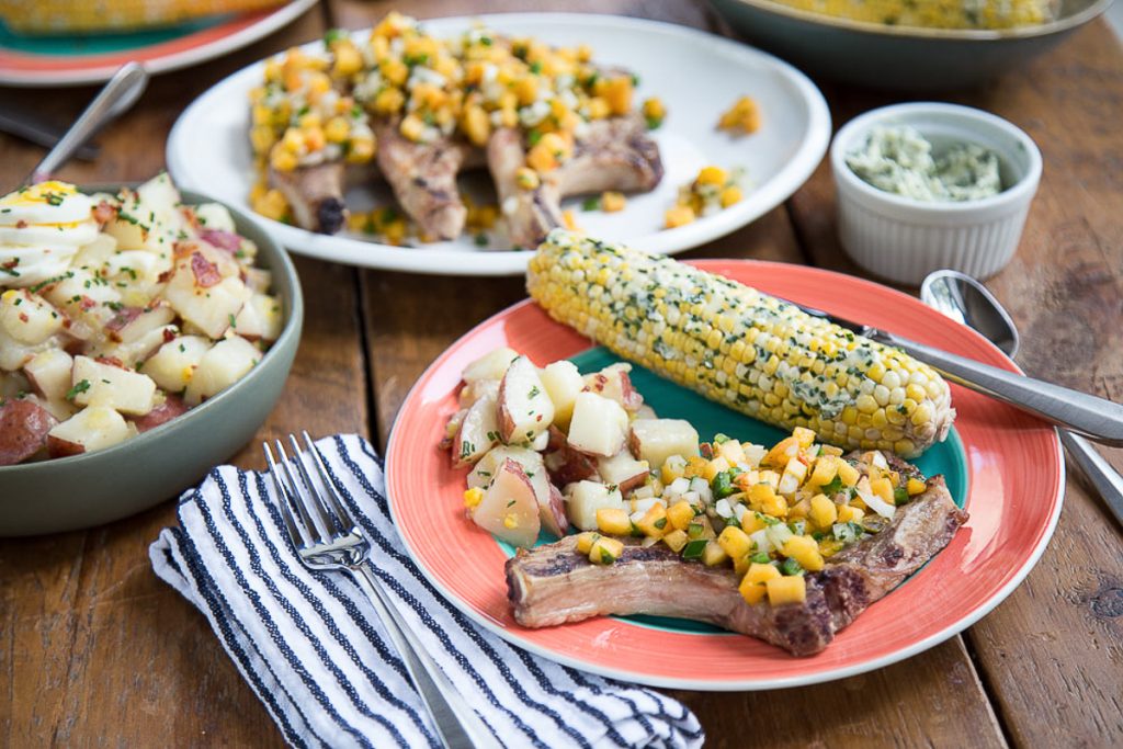 summer meal with pork chops, corn, and potato salad on a wooden table