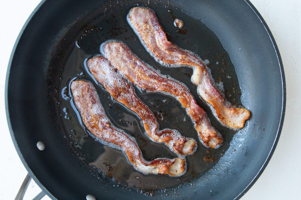 four slices of bacon cooking in a nonstick skillet