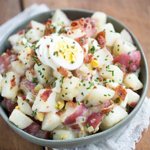 German potato salad with hard boiled eggs and chives in a green bowl on a wooden table