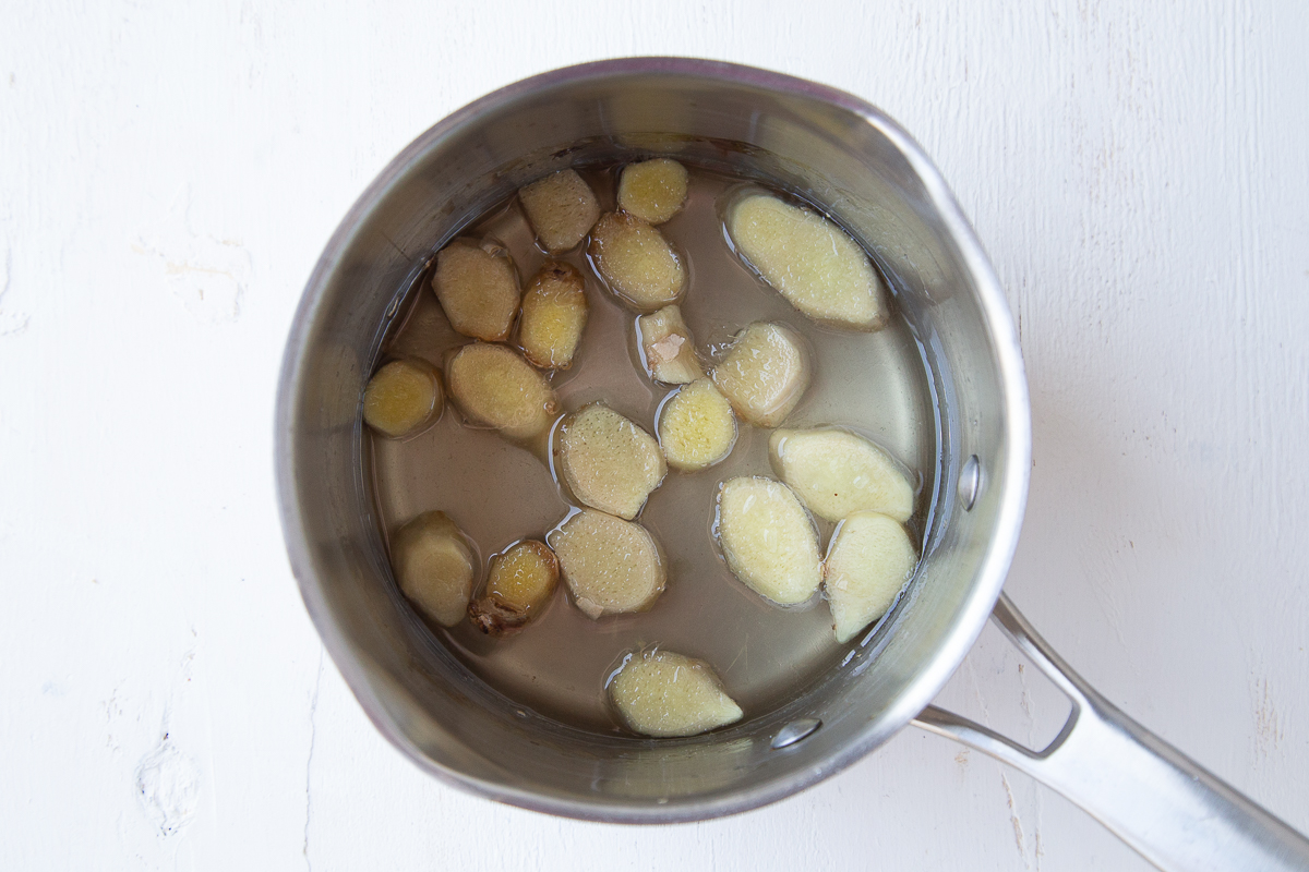 coins of ginger sitting in simple syrup in a small saucepan